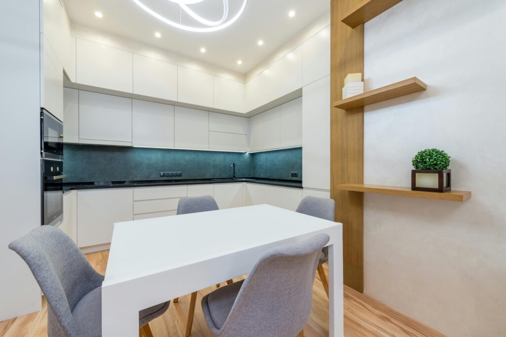 Modern apartment interior with table with chairs next to shelves and open kitchen with cabinets