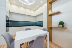 Modern apartment interior with table with chairs next to shelves and open kitchen with cabinets