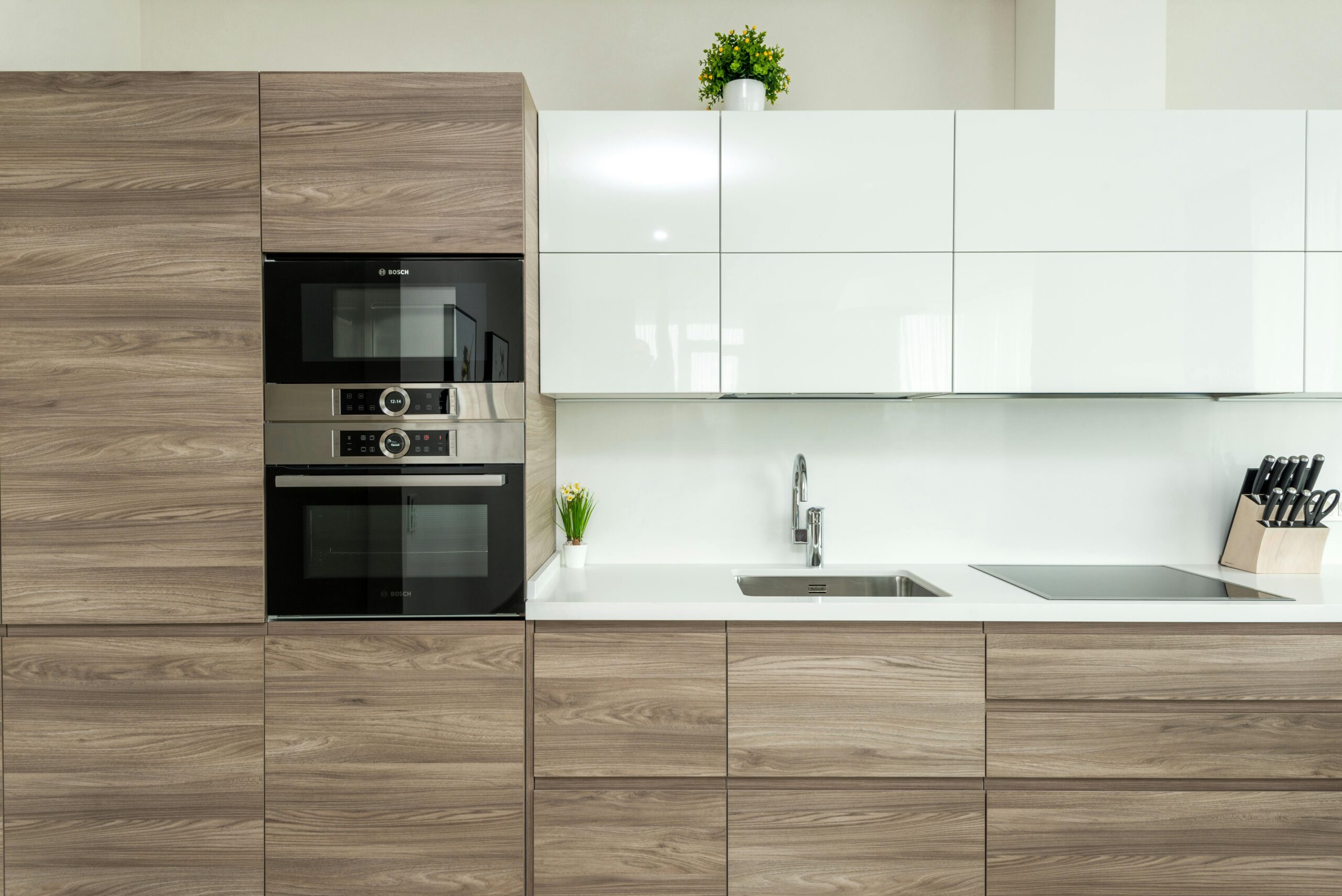 Interior of modern kitchen with white and wooden minimalist cabinets and built in appliances in apartment
